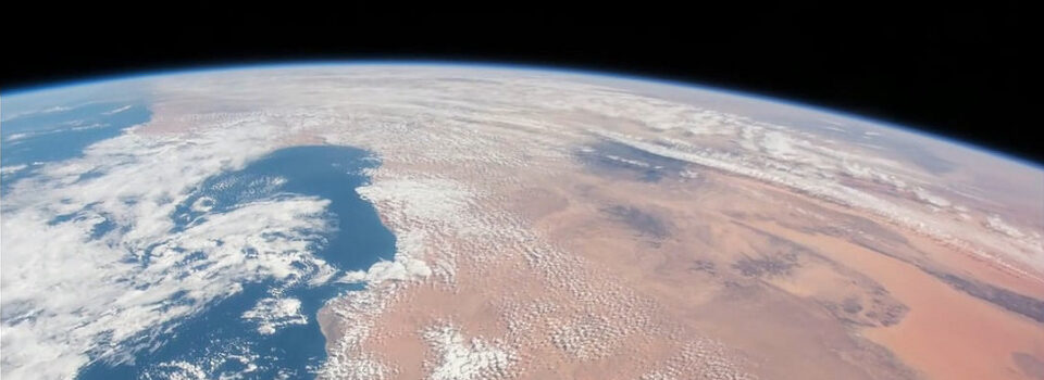 Blick auf Libyen aus dem Weltall mit Sahara-Wüste und Wolken über dem Mittelmeer, blauem Himmel und Erdkrümmung im Hintergrund.